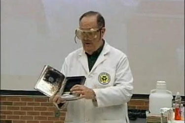 Man in lab coat showing a book with charred pages